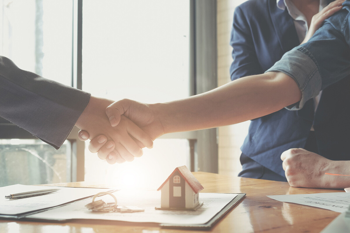 A St. Louis homebuyer shaking hands at a closing, with house keys and a model home on the table.